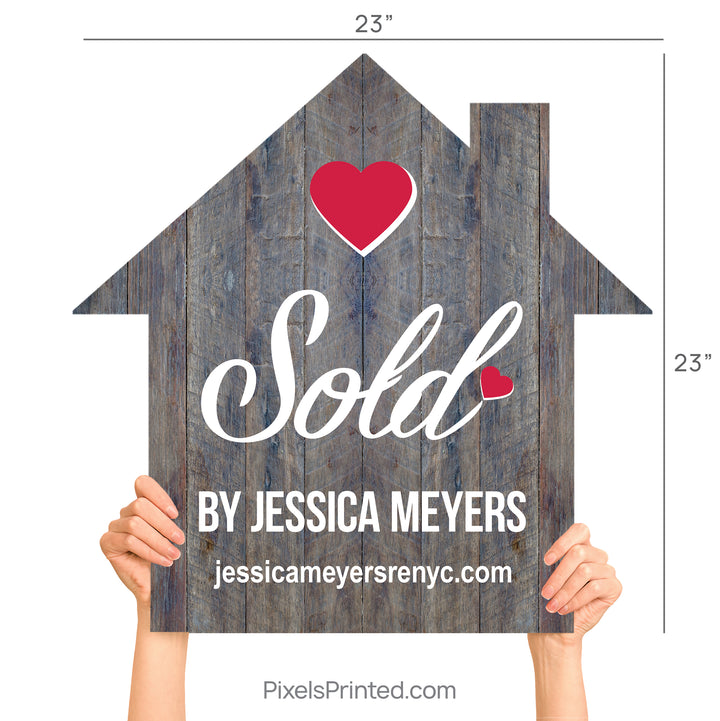 A realtor holding a wooden house-shaped sign that says Sold By during a client closing.